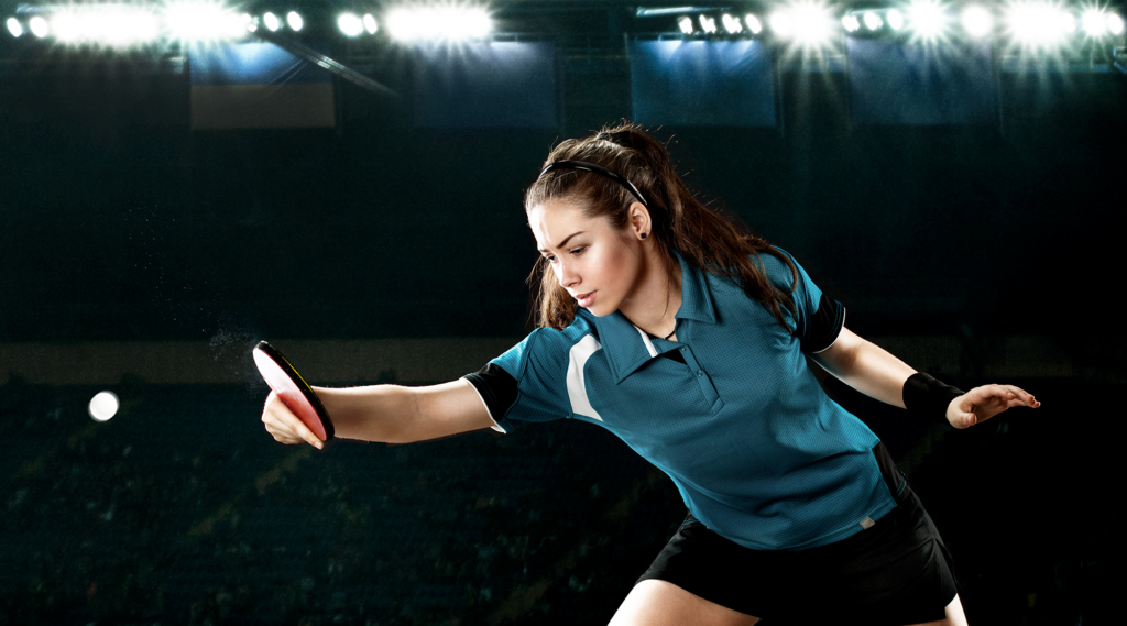 A women with a green t-shirt hitting a ping pong ball.