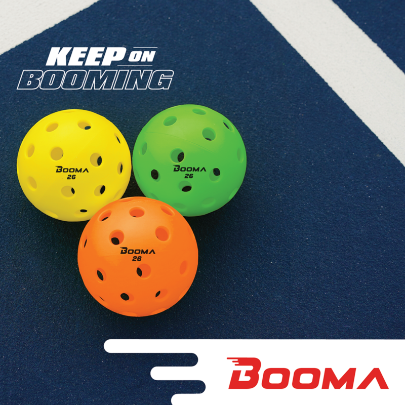 Image of BOOMA 26 indoor pickleball balls in orange, green and yellow. Balls are on a pickleball court.