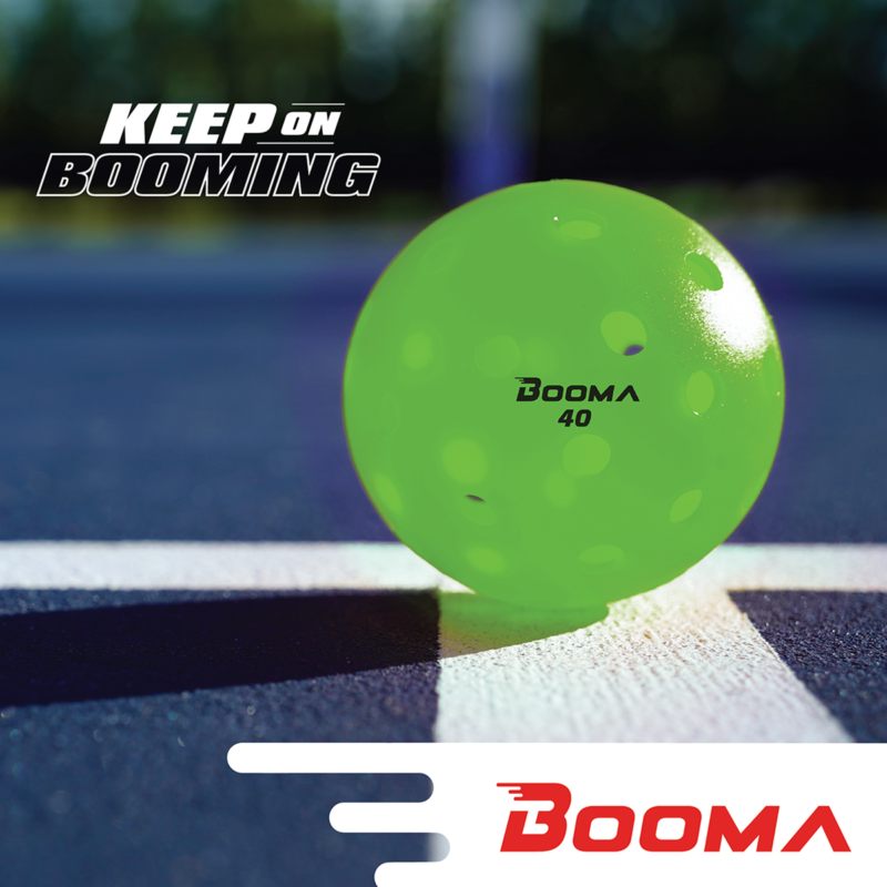 A close up of a green BOOMA 40 outdoor pickleball ball on a court.