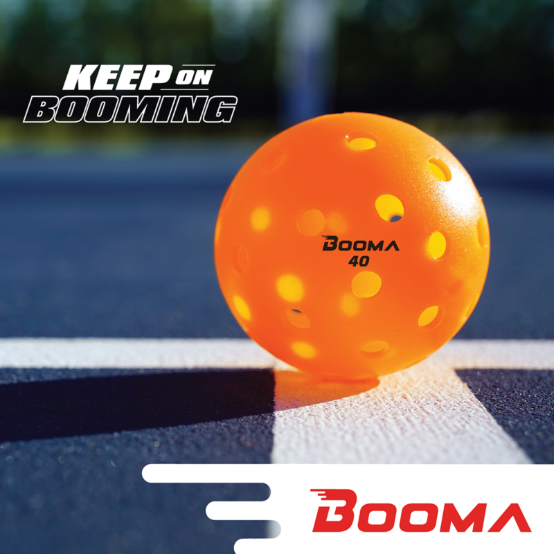 A close up of an orange BOOMA 40 outdoor pickleball ball on a court.