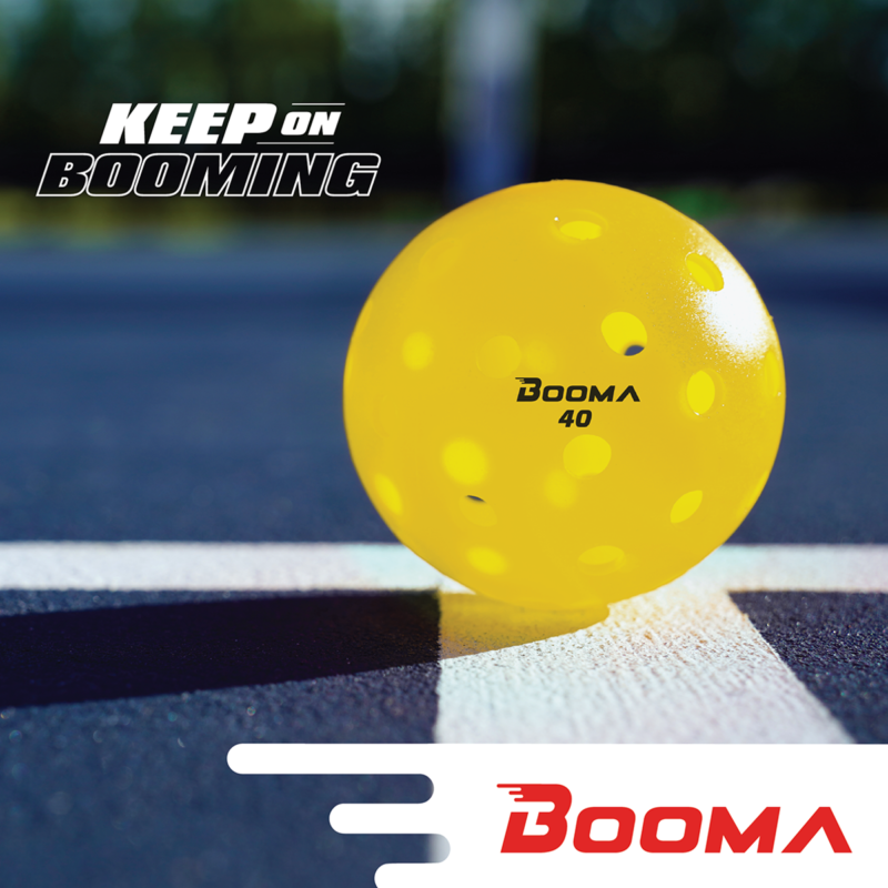 A close up of a yellow BOOMA 40 outdoor pickleball ball on a court.